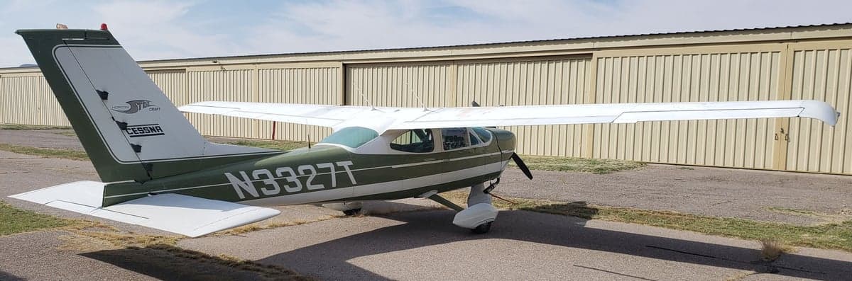 A Cessna aircraft with a green and white paint scheme is parked on the pavement.