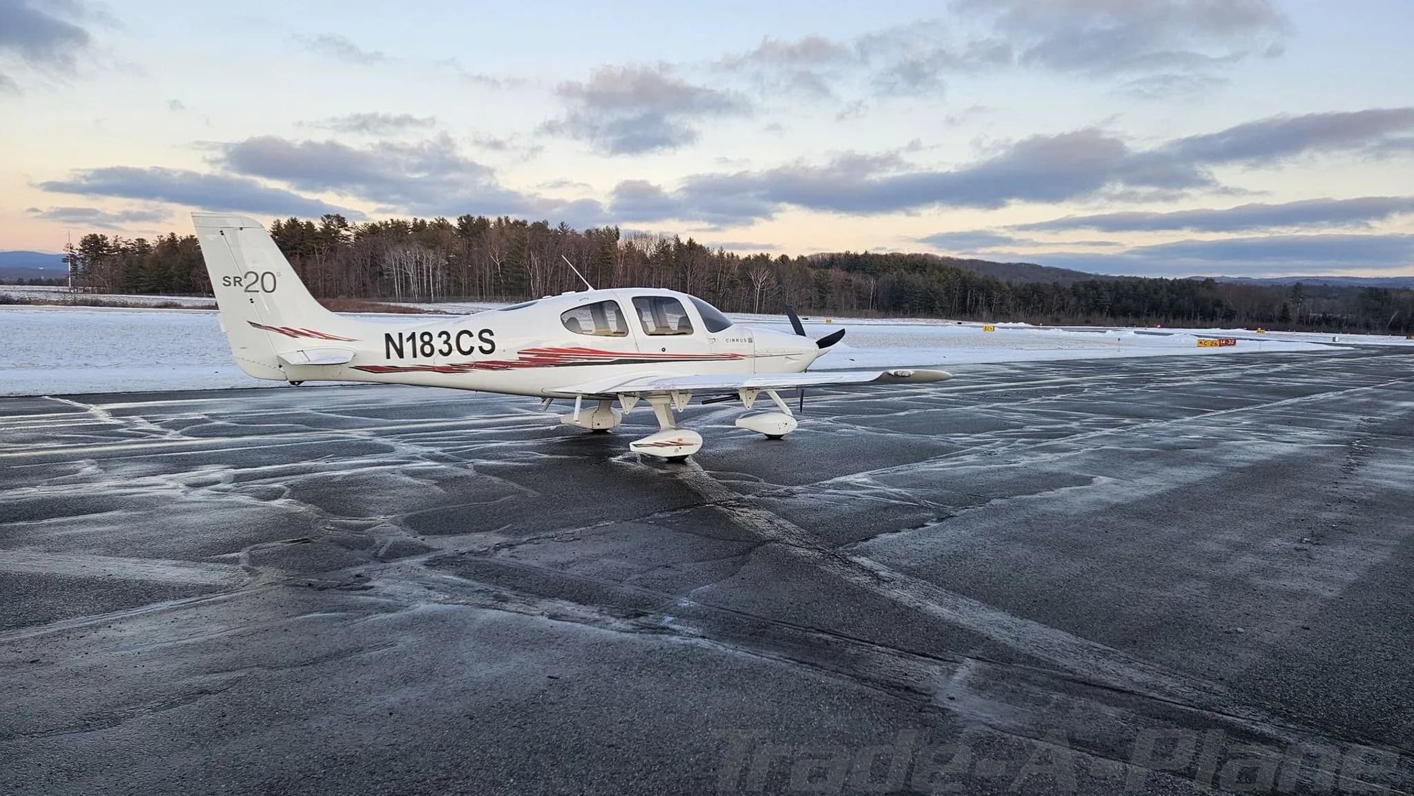 Rear-side view of a white Cirrus SR20 aircraft with red and black stripes on a wet tarmac.
