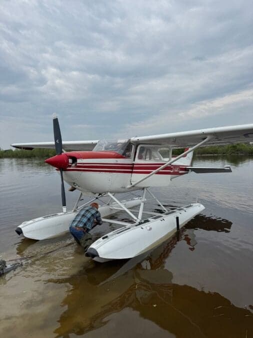 A Cessna floatplane with red and white paint scheme is being pulled from the water.