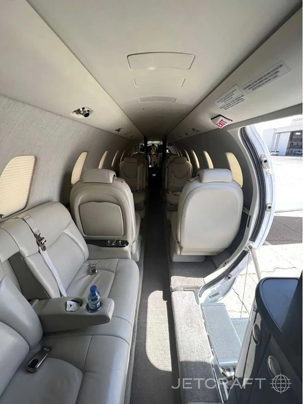 The interior of a private jet cabin features light-colored leather seats and a narrow central aisle.