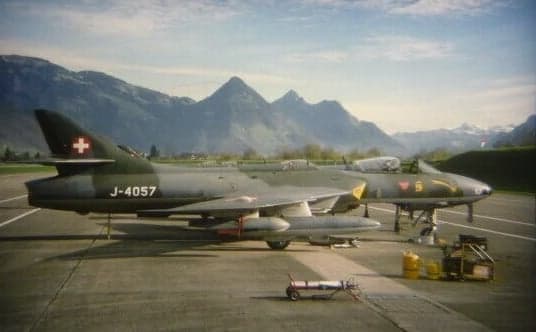 Two Swiss Air Force Hawker Hunter aircraft, registration J-4057, parked on the tarmac with mountains in the background.