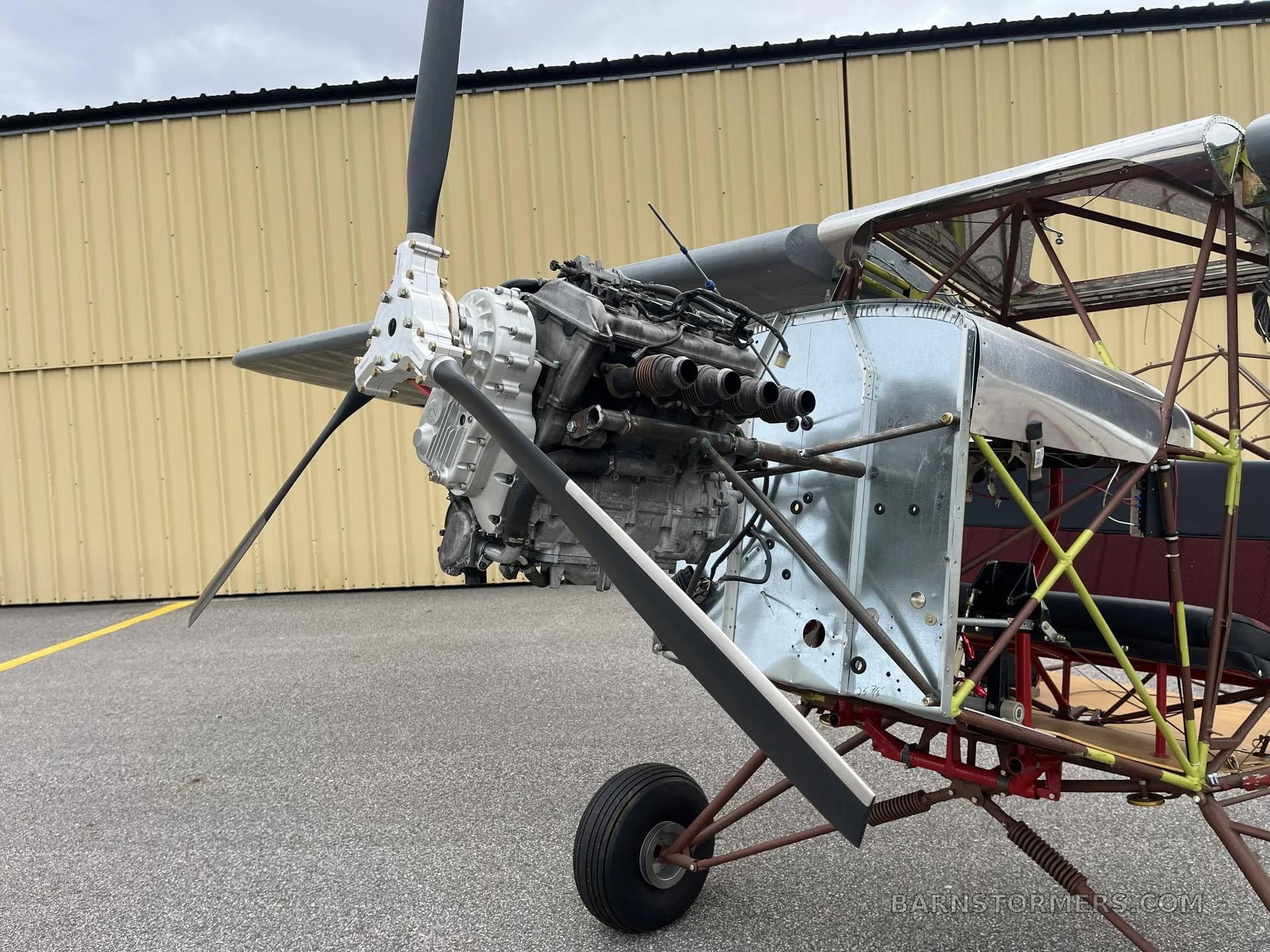 A close-up view of the exposed engine and propeller of an ultralight aircraft, with the front landing gear visible.