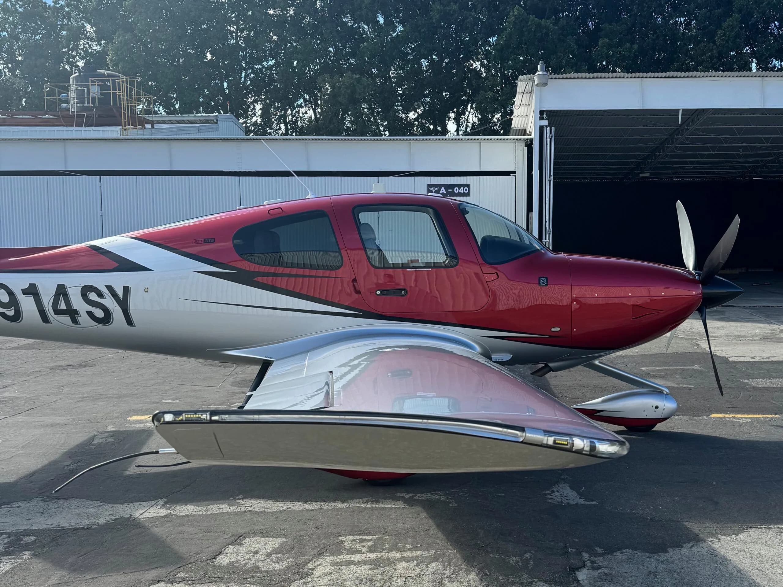 A side view of the red and silver Cirrus SR22 aircraft N914SY, showing its wing and fuselage.