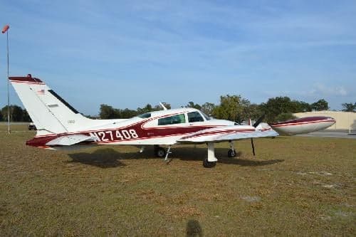A Beechcraft Baron with a white and maroon paint scheme is parked on the grass.