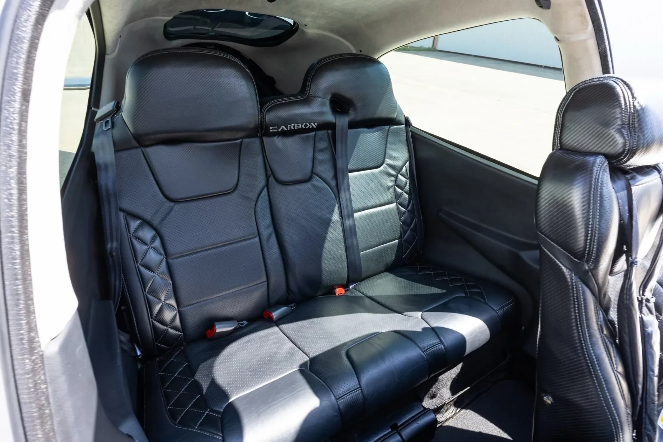 The rear cabin of a Cirrus SR22 aircraft, featuring two black quilted leather seats with "CARBON" embroidered on them.