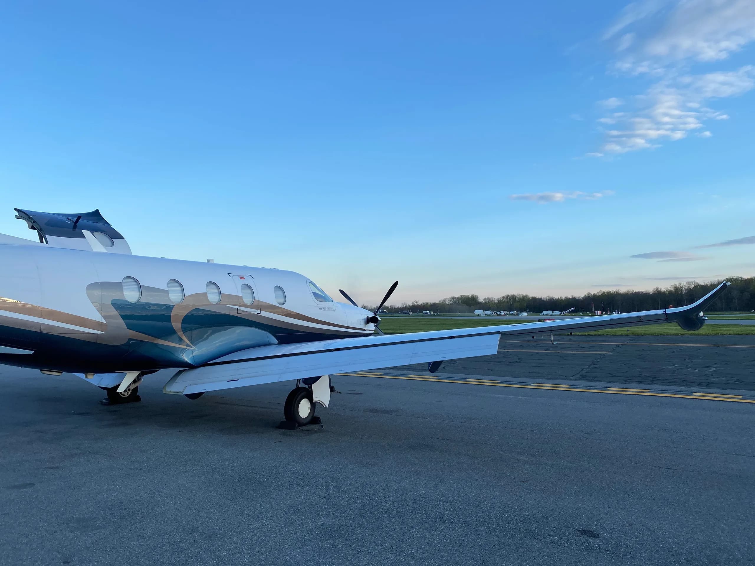 A Pilatus PC-12 aircraft is parked on the tarmac with a blue and brown paint scheme.