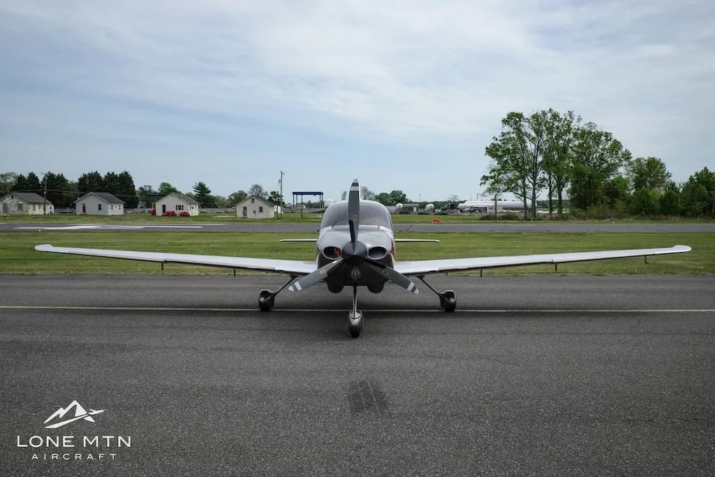 Front view of a silver and orange Cirrus SR22 aircraft with a three-bladed propeller, parked on an asphalt runway.