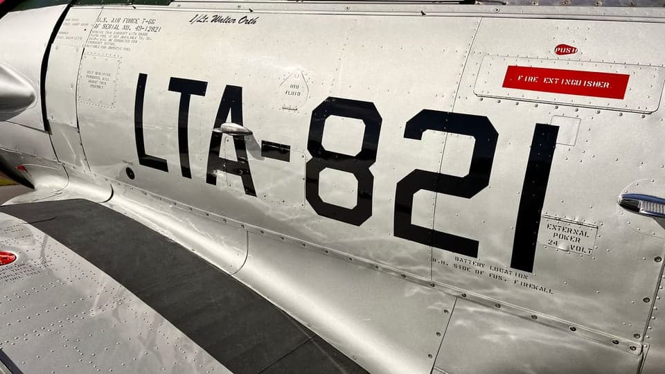 A T-6 Texan aircraft with a silver and red paint scheme parked on the tarmac.