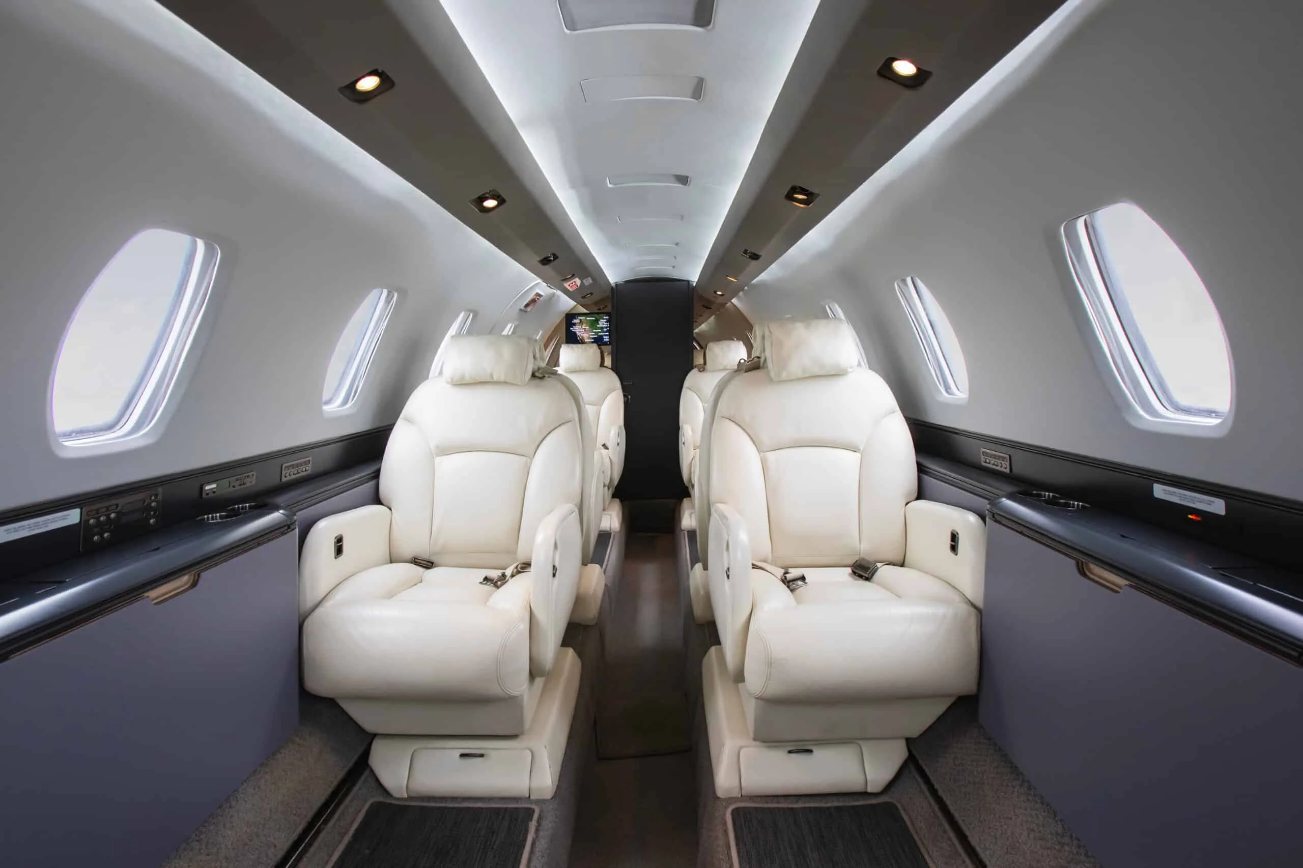 The luxurious interior of a private jet cabin with light-colored leather seats and overhead lighting.