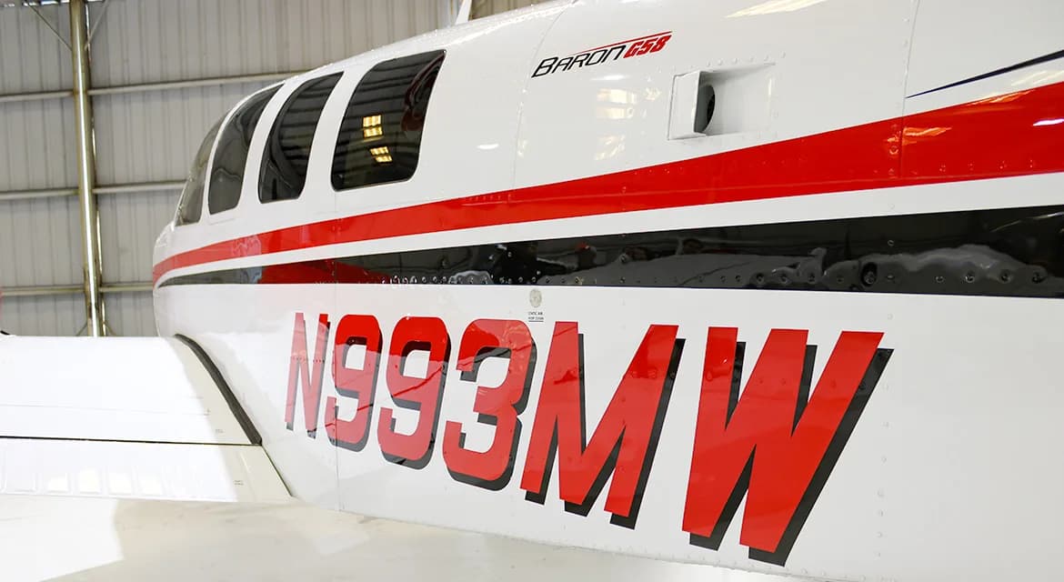 A close-up of the fuselage of a white and red Beechcraft Baron G58, showing the tail number N993MW.