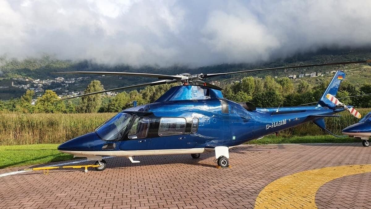 A blue AgustaWestland AW109SP helicopter, registration D-HABM, is parked on a helipad.