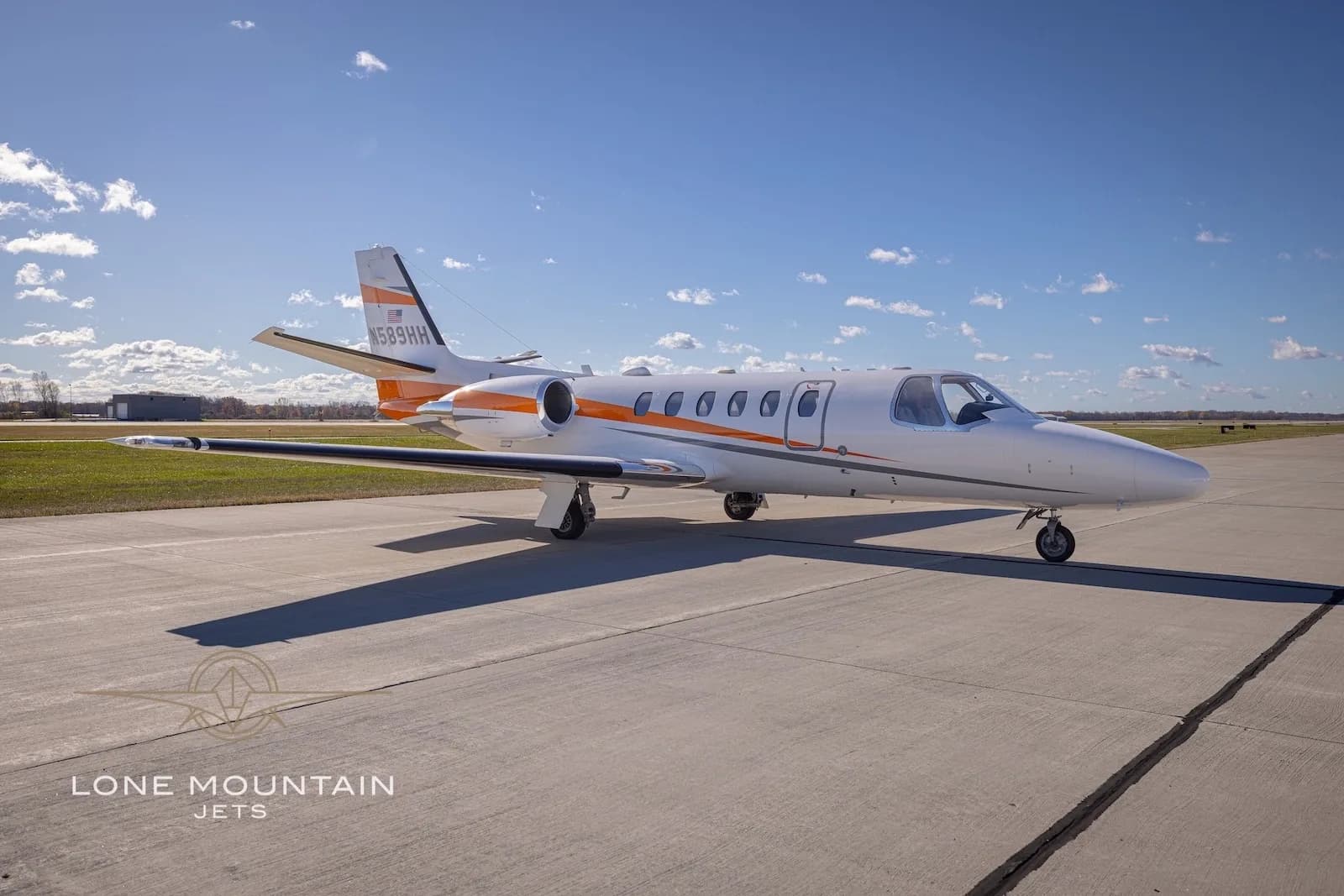 A three-quarter front view of the white Cessna Citation Bravo business jet N589HH on the tarmac under a partly cloudy sky.