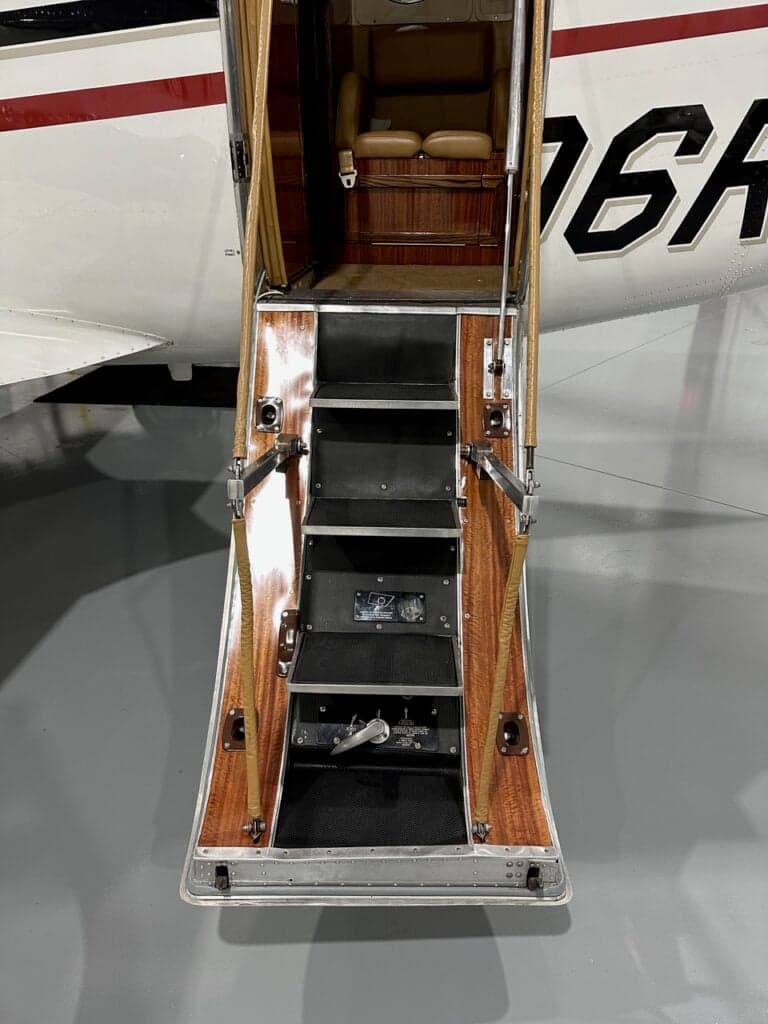 The open airstair door of the aircraft, showing wooden steps and handrails leading into the cabin.