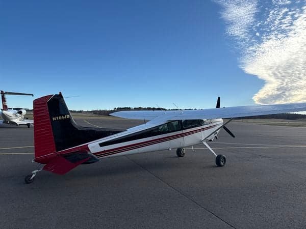 Side view of a Cessna 185 Skywagon parked on the tarmac, with another aircraft visible in the background.