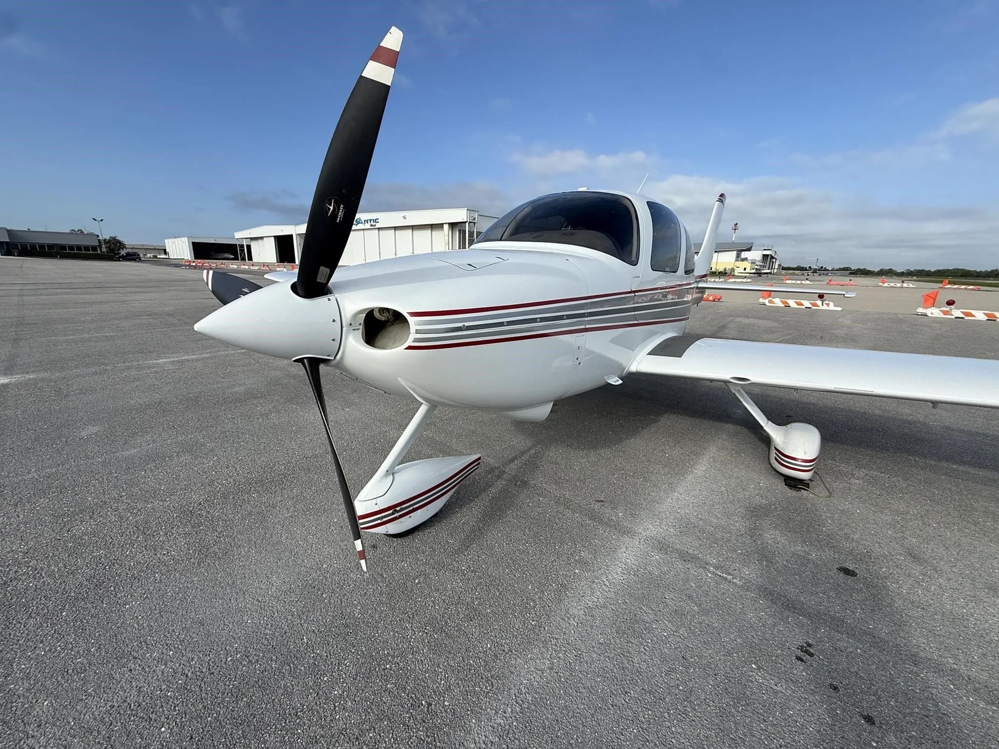 A close-up front view of a white Cirrus SR22 aircraft with red and gray stripes, tail number N88BM, showing the propeller and nose.
