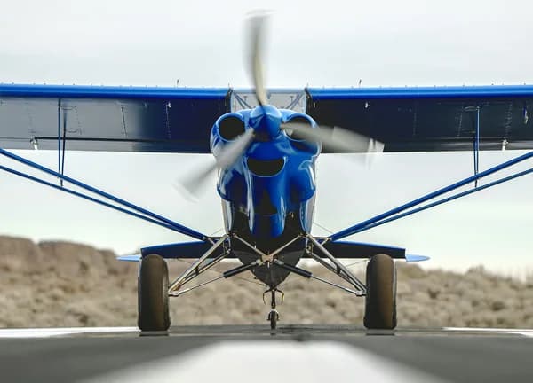 Front view of a blue aircraft with a spinning propeller on a runway.