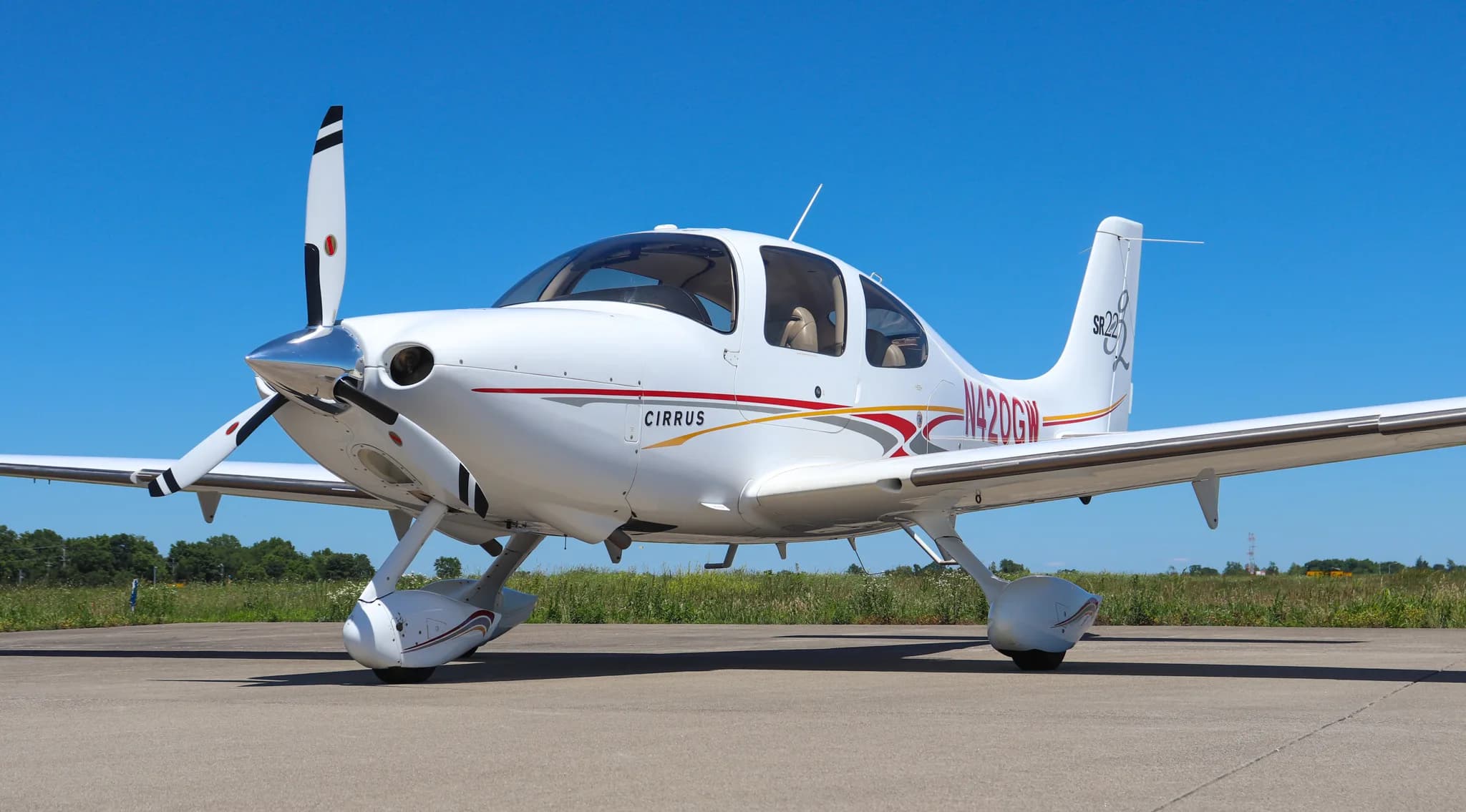 Front-left view of a white Cirrus SR22 aircraft with red and gold stripes on a tarmac under a clear blue sky.