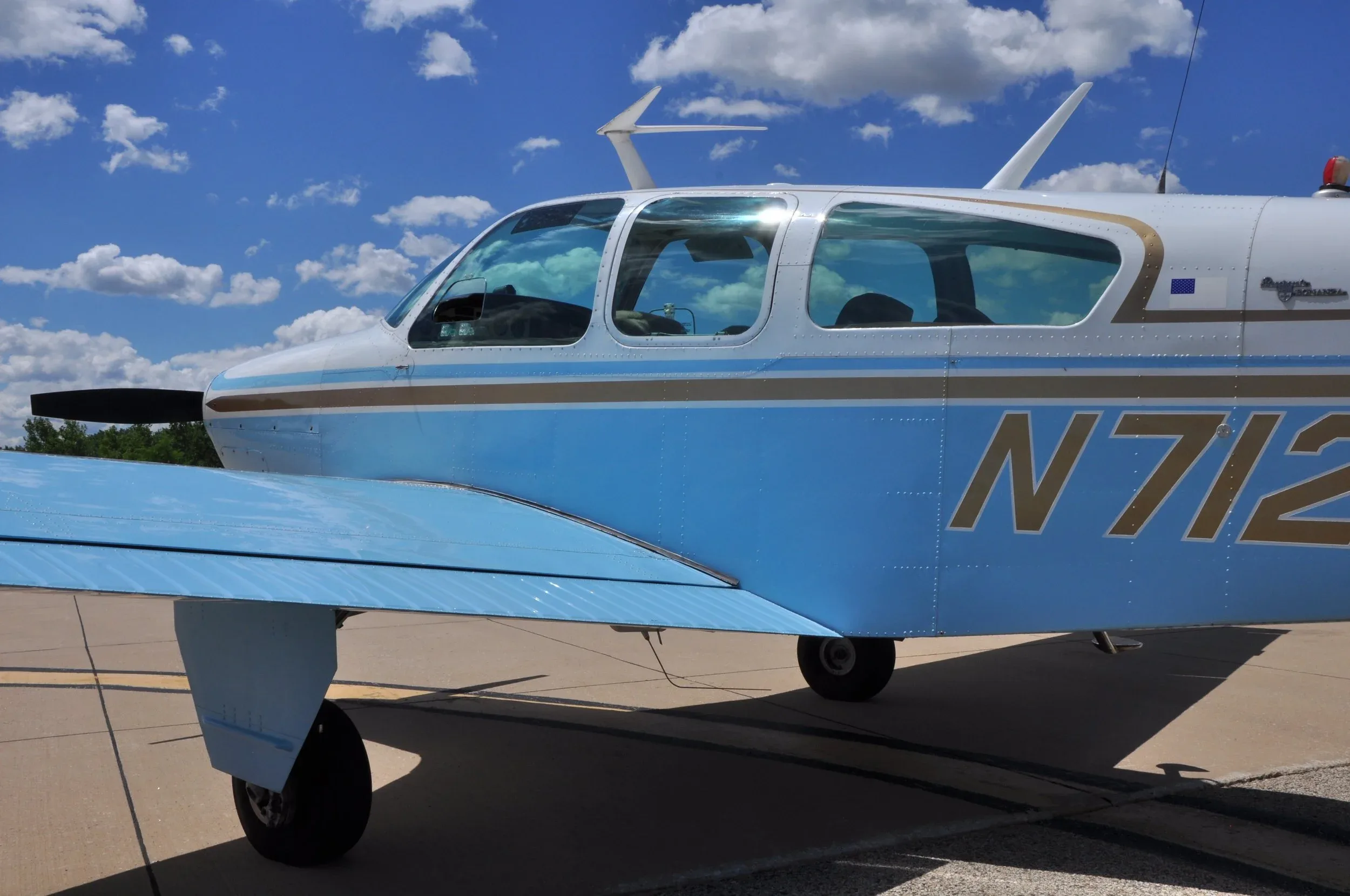 A close-up view of the cockpit windows and wing of a light blue and white single-engine aircraft, showing the registration N7128N.