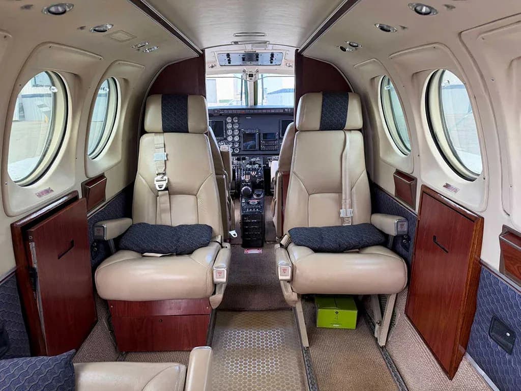 The interior cabin of a Beechcraft King Air C90GTx, showing two beige passenger seats facing the cockpit.