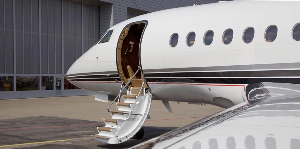 A white business jet with a black and grey stripe, parked on an tarmac with its main entry door open and stairs extended.