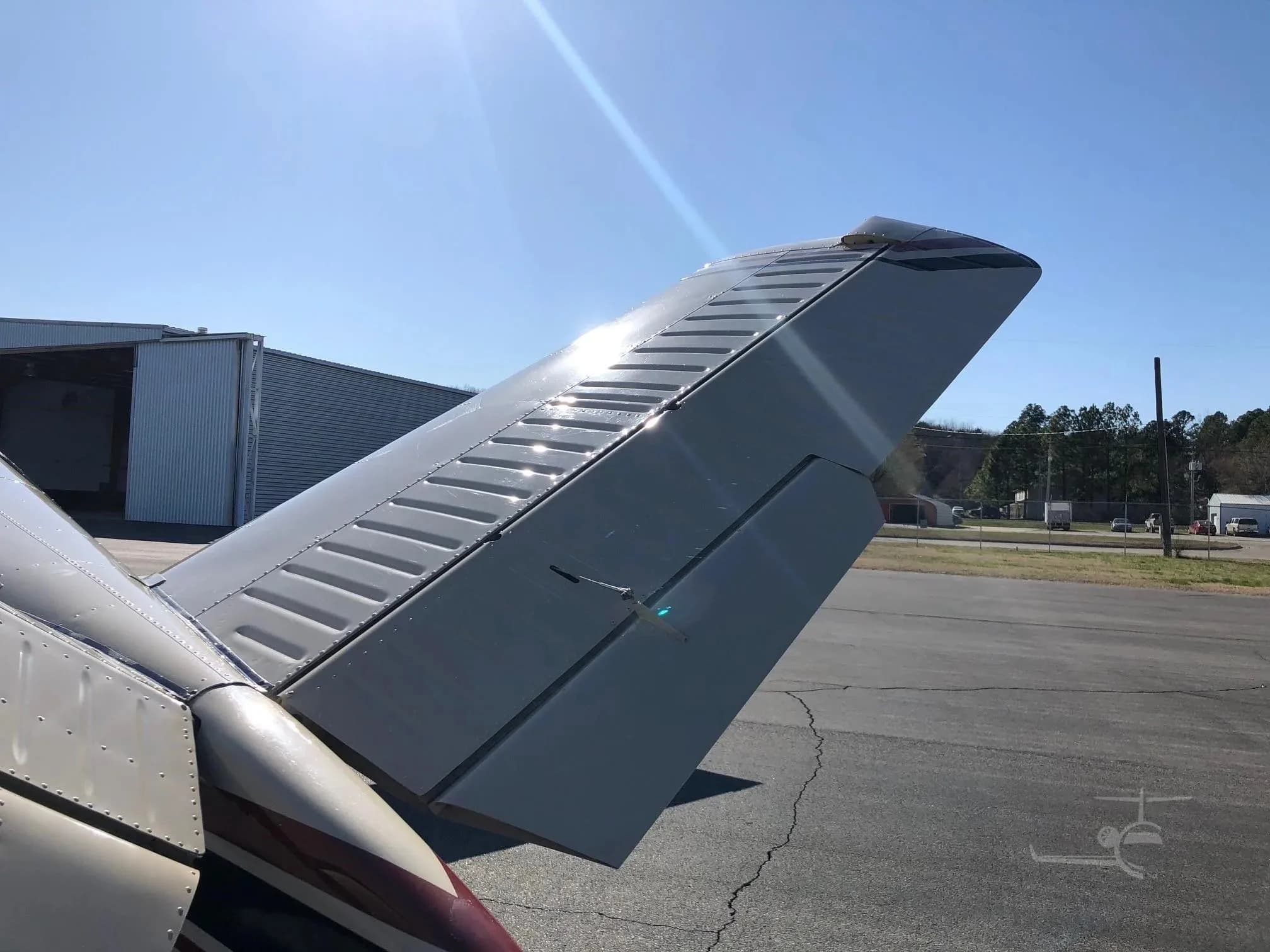 A close-up view of the V-tail of the beige Beechcraft Bonanza N980Q, showing the control surfaces.