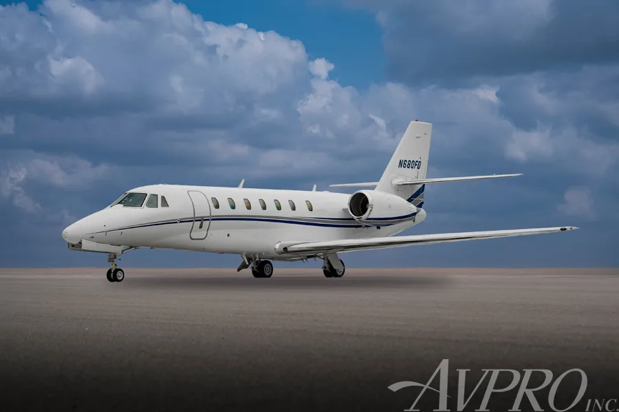 A side view of the white Cessna Citation Sovereign (N680FD) with blue and grey stripes, parked on a tarmac under a cloudy blue sky.