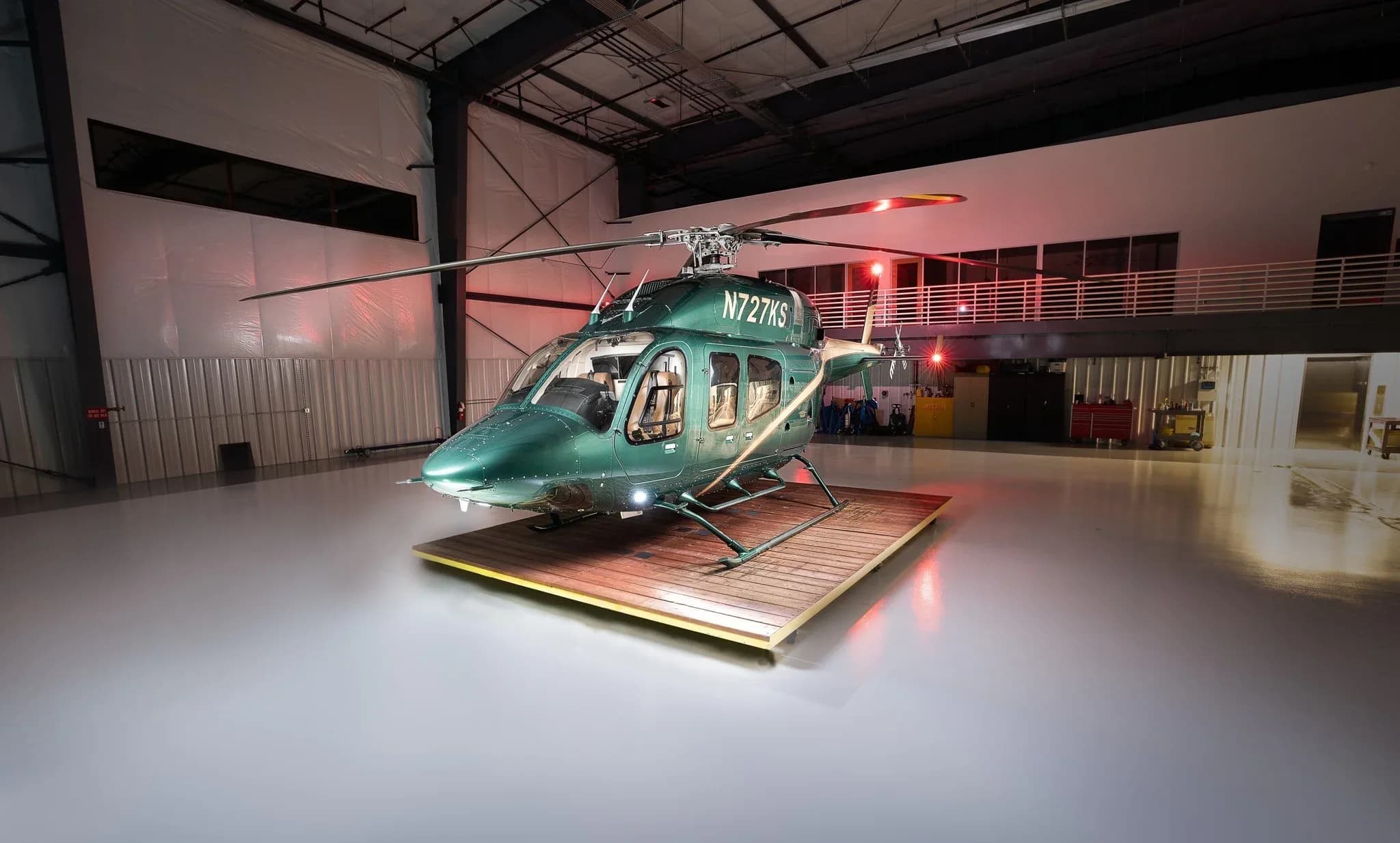 Front view of a green Bell 407 helicopter with registration N727KS inside a hangar.