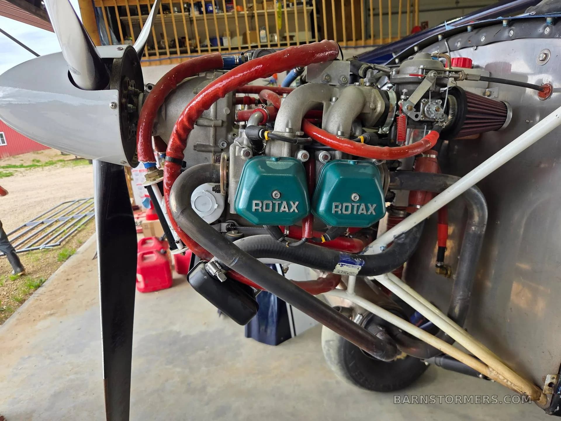 A Rotax aircraft engine with green valve covers and a propeller is shown from the front in a hangar setting.
