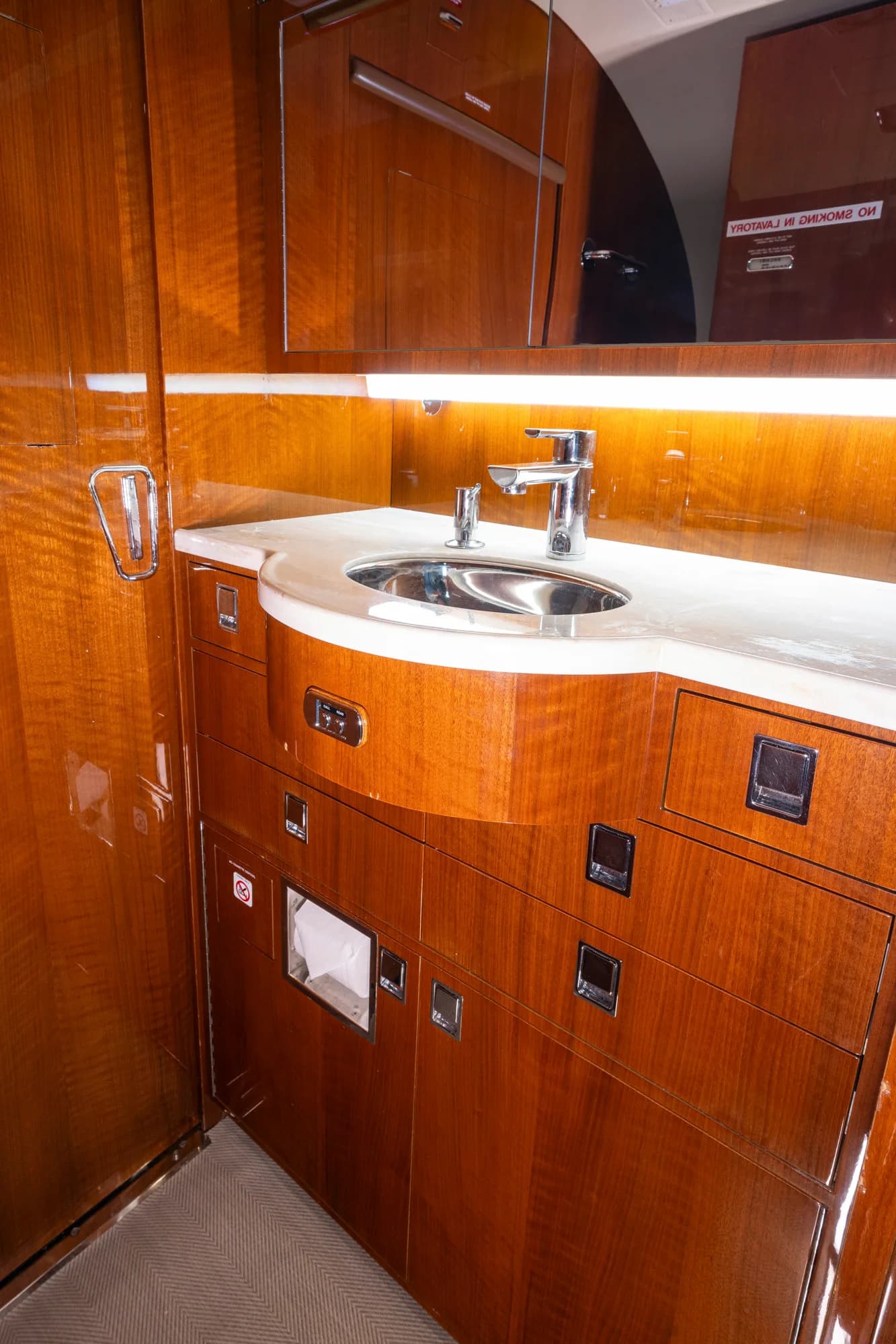 A close-up of the sink and polished wood cabinetry in the business jet's galley or lavatory.