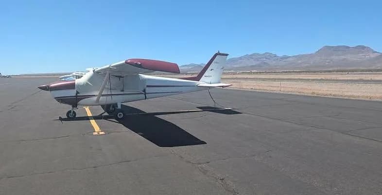 A side view of the white and maroon Cessna 172M, N8452X, parked on an airfield with mountains in the distance.