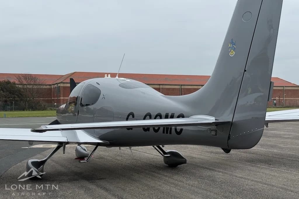 A rear view of the silver Cirrus SR22 aircraft, showing its tail and registration G-GOMC, parked on an airfield.