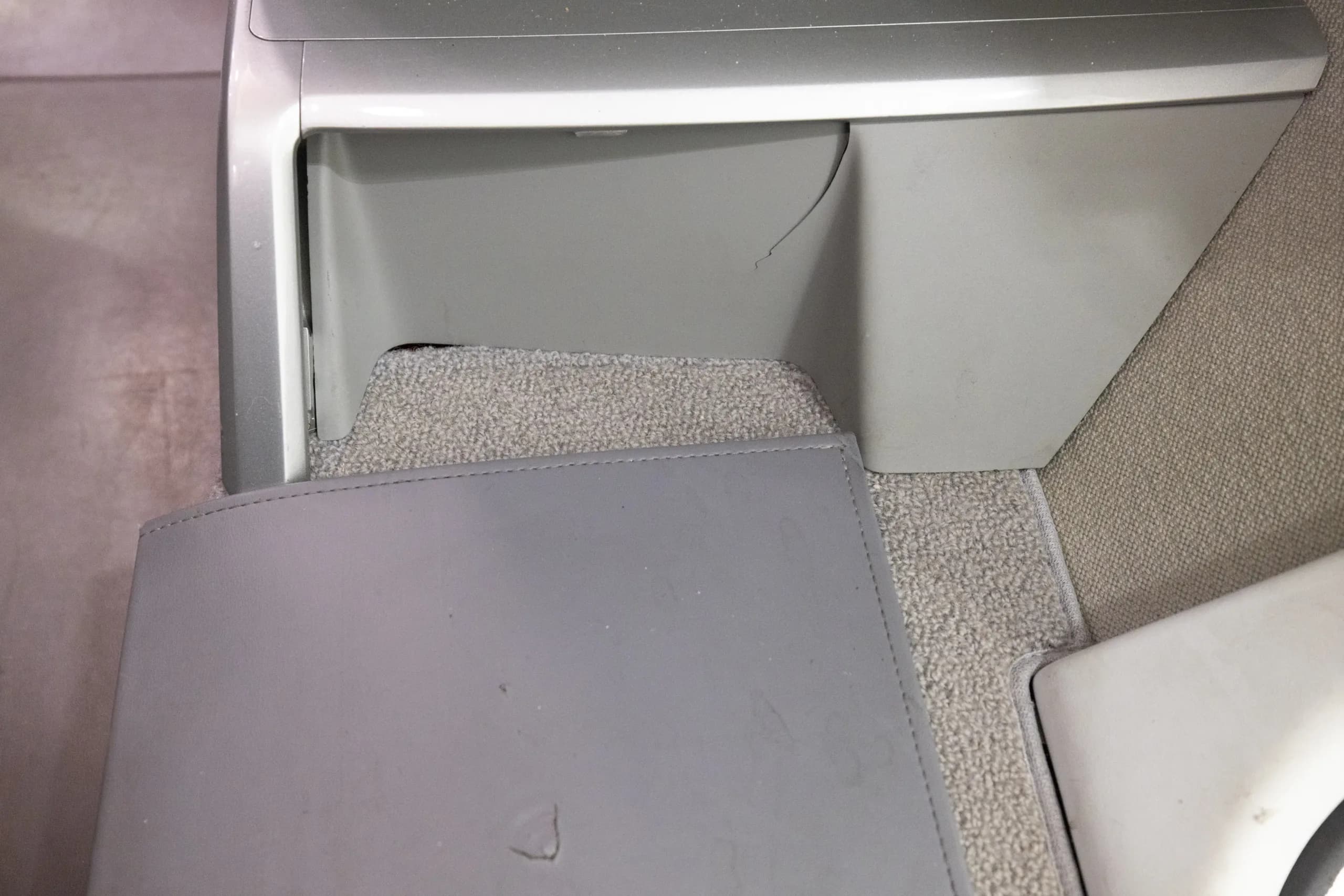 A close-up view of the light gray carpet and a small storage compartment in an aircraft cabin.