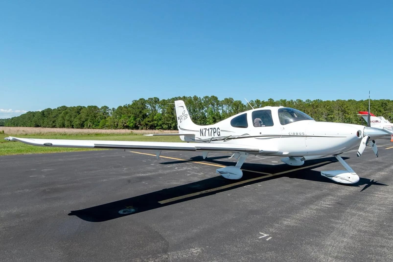 Side view of a white Cirrus SR22T aircraft N717PG with black and grey stripes parked on an airfield.
