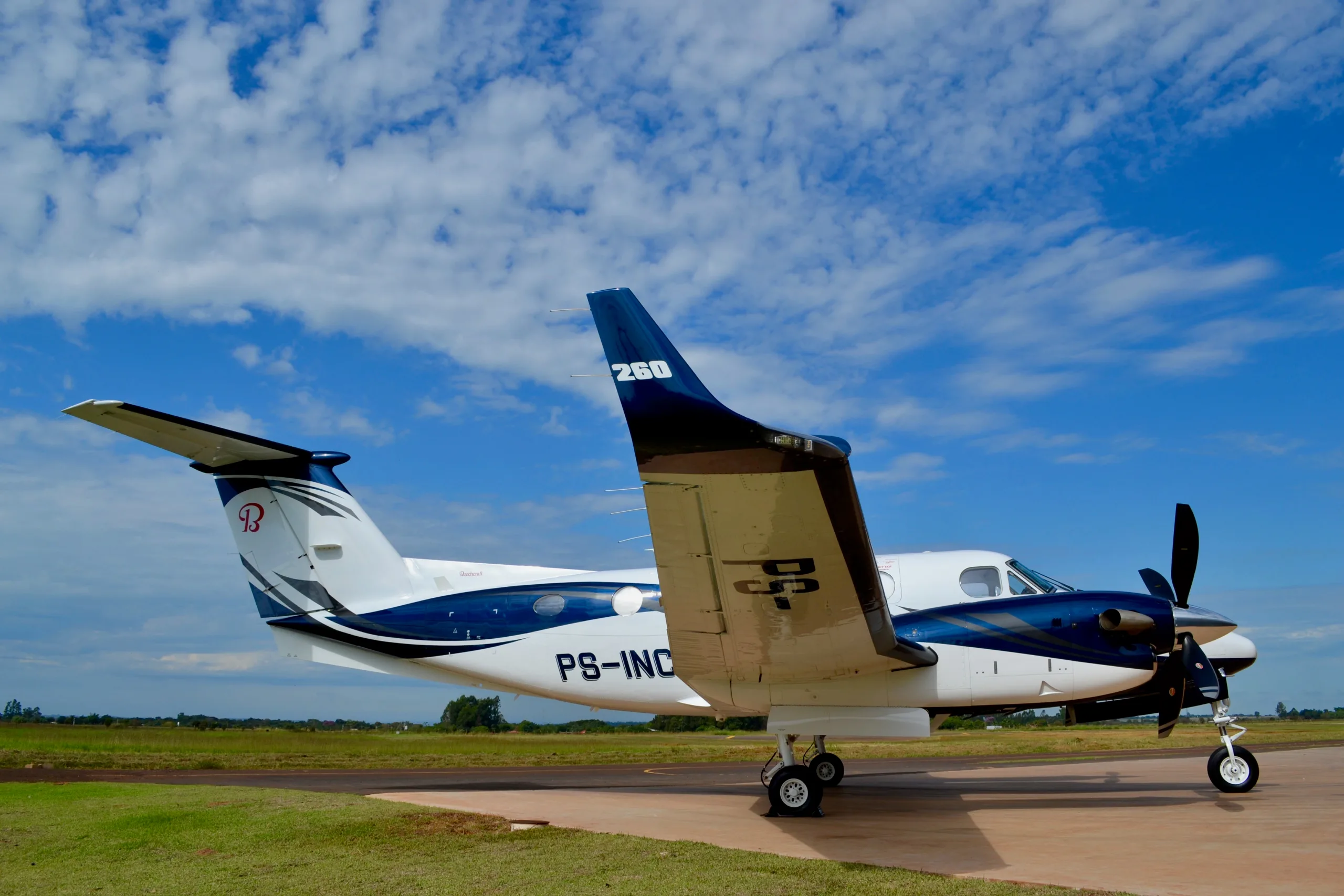 A side view of a white and blue twin-turboprop aircraft, registration PS-INC, parked on a tarmac.