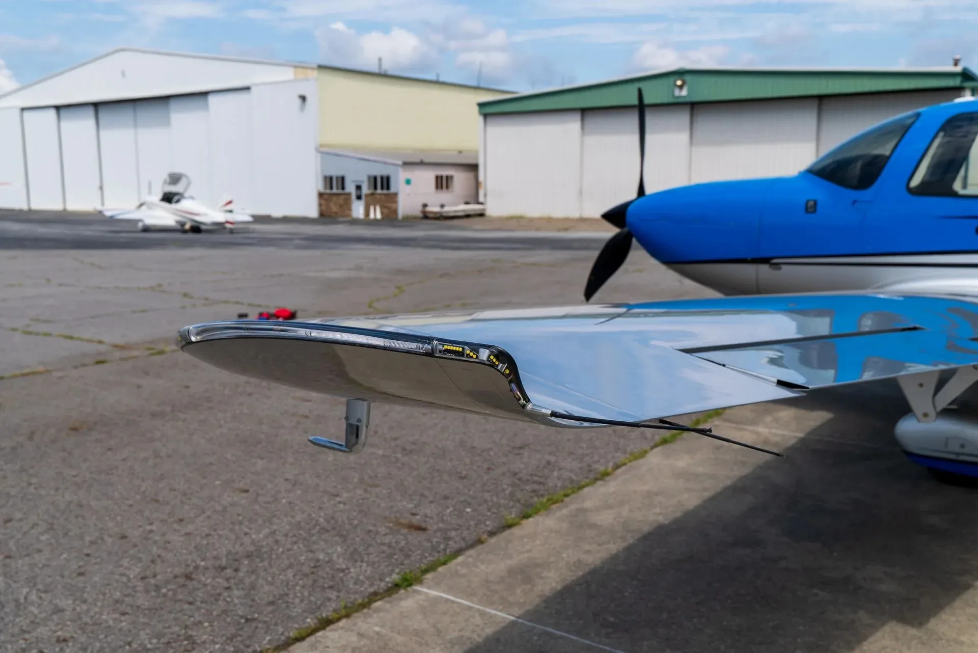 A close-up view of the wingtip and propeller of a blue and silver Cirrus SR22 aircraft on an airfield.