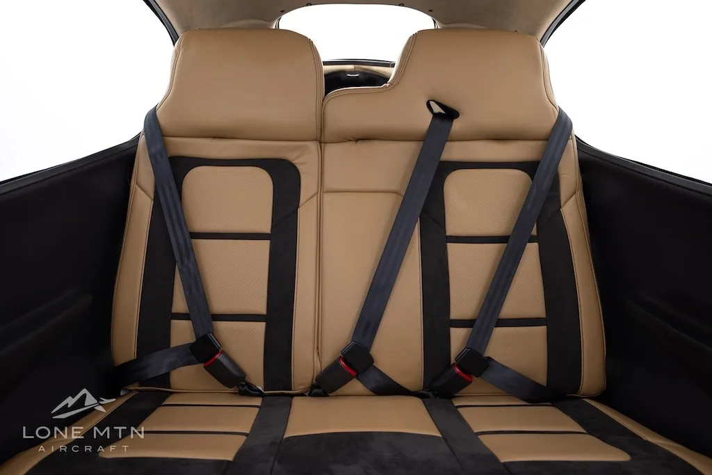 The tan and black leather rear seats of the aircraft cabin with seatbelts fastened.