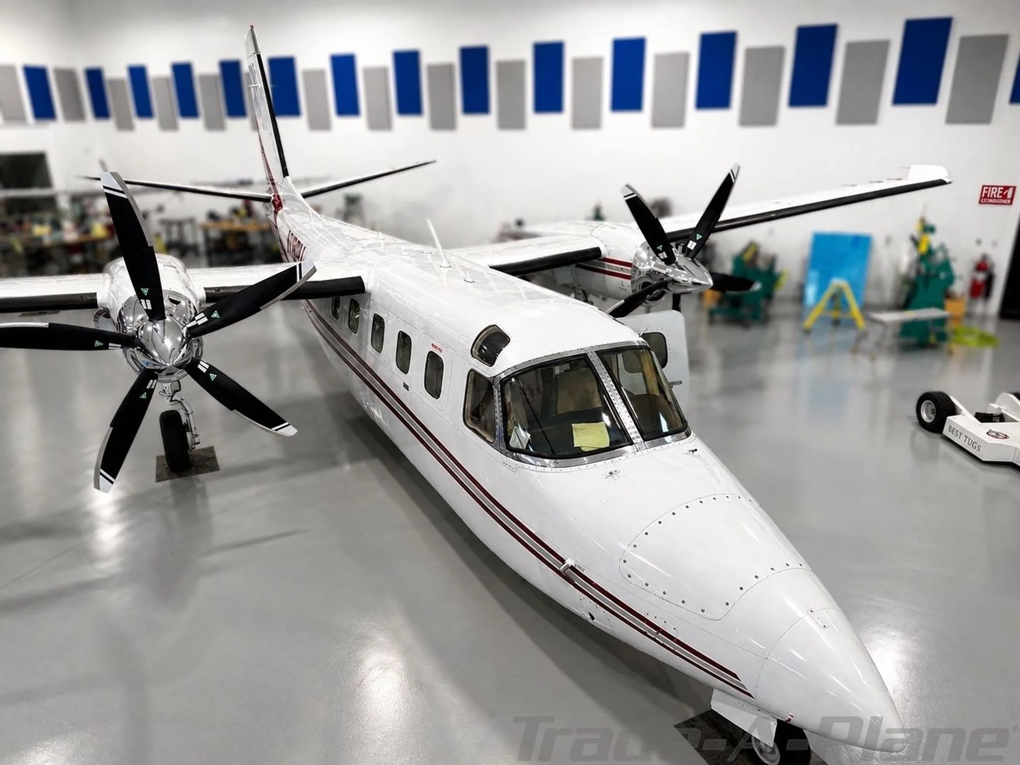 A white twin-engine turboprop aircraft with red stripes, seen from the front-right in a hangar.