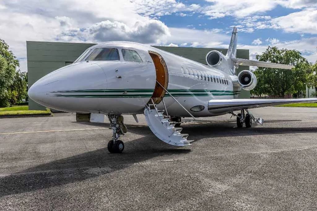 A white Dassault Falcon 900EX with its main cabin door open and stairs extended on an airfield.