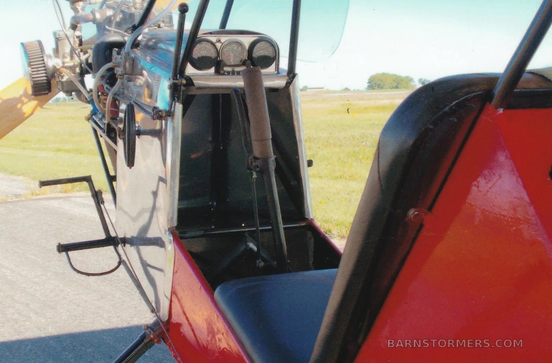 A close-up view of the open cockpit of an ultralight aircraft, showing the seat, control stick, and basic instruments.
