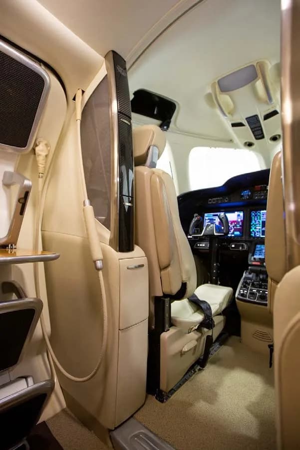 A close-up view of a cabin seat and an entertainment or storage unit, with the cockpit visible in the background.