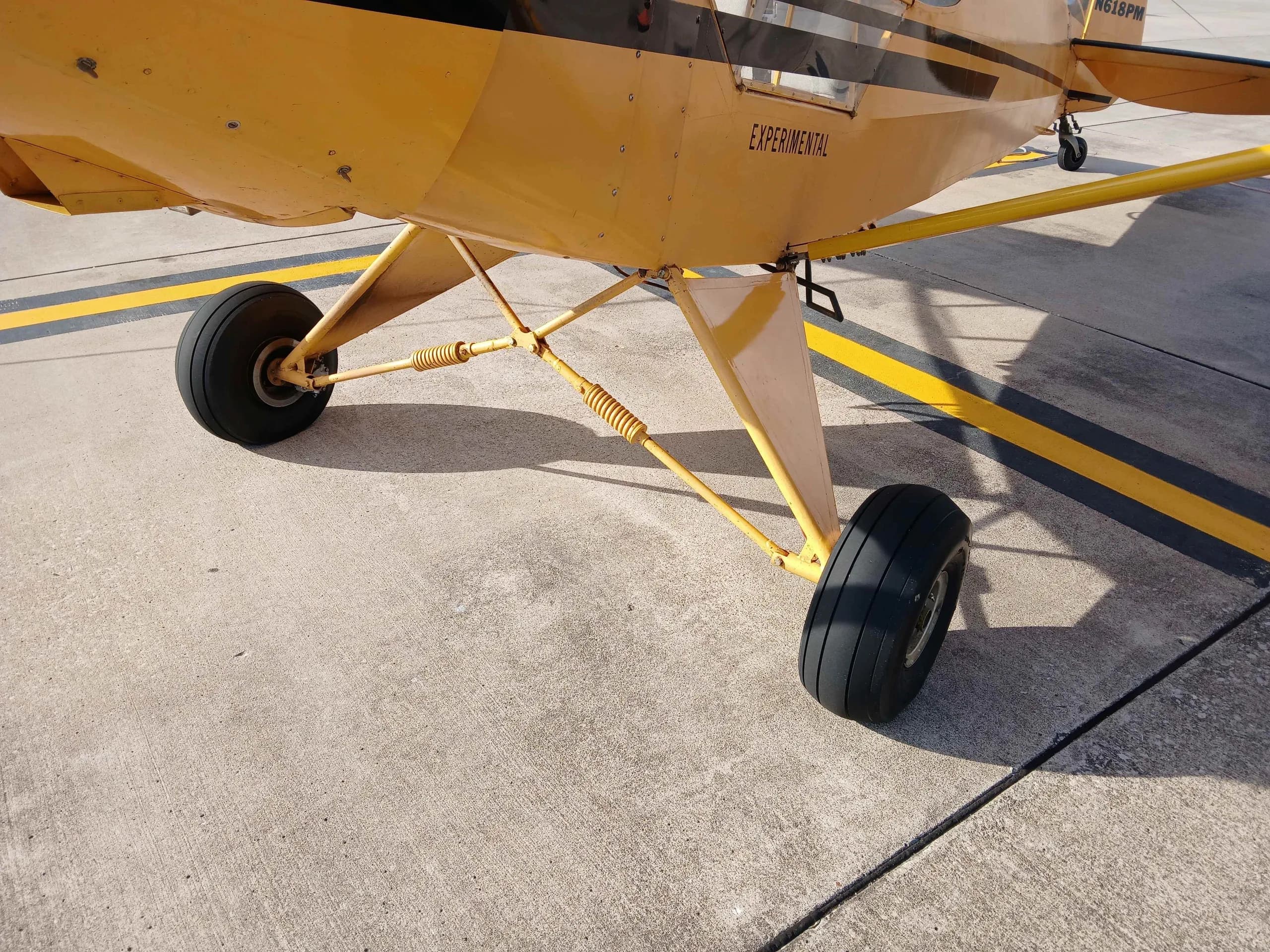 Close-up view of the main landing gear and fuselage of the yellow N618PM aircraft on asphalt.
