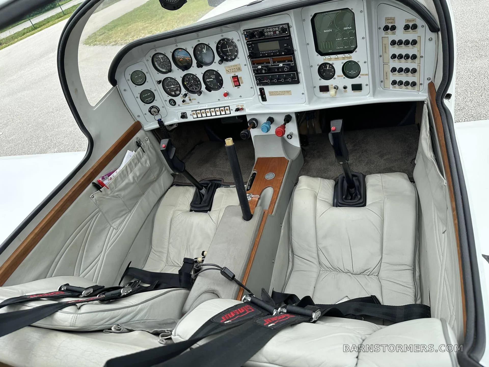 Overhead view of a white aircraft cockpit with a detailed instrument panel and two white leather seats.