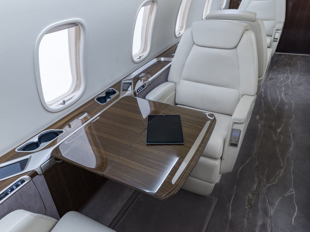Close-up of a white leather seat and wood table in the aircraft's interior.