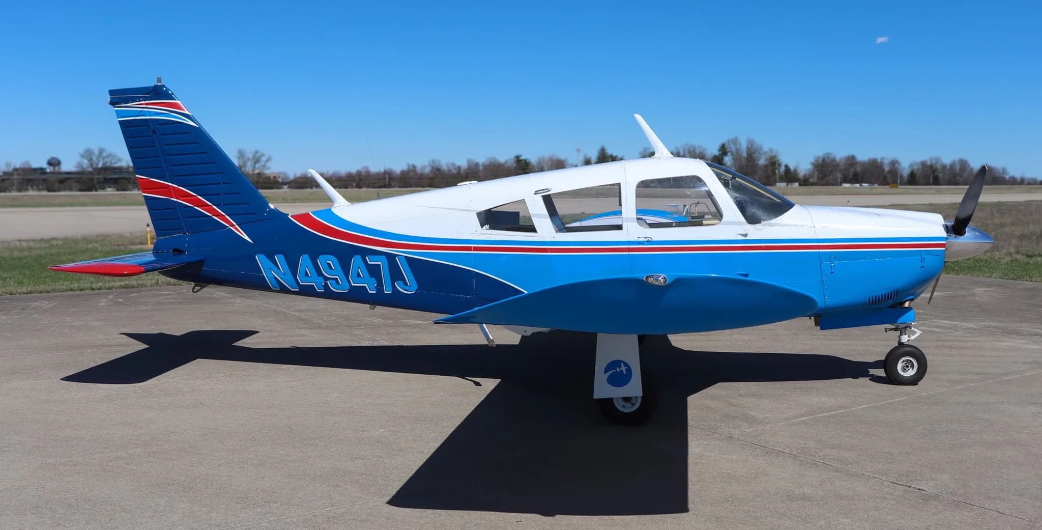A side view of a blue and white Piper Cherokee aircraft with red stripes parked on an airfield.