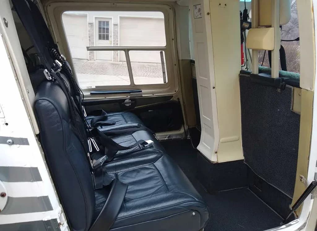 Interior view of the helicopter cabin showing black leather rear seats and the open side door.