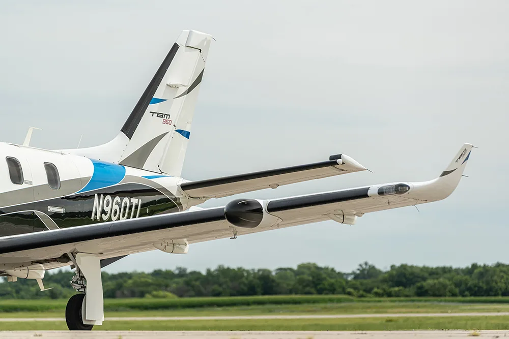 A rear-side view of a white, blue, and black TBM 960 turboprop aircraft with registration N960TL on an airfield.