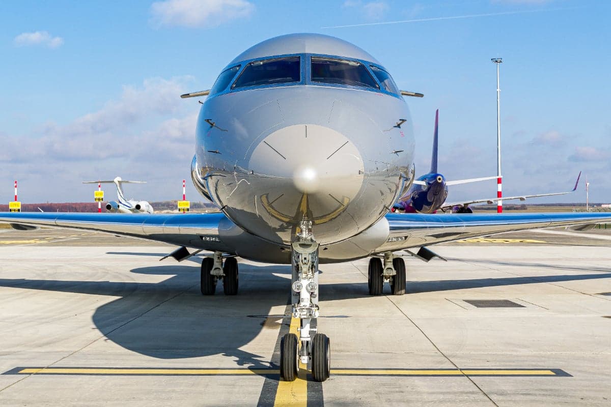 A front view of the Bombardier Global 5000 aircraft 9H-ARE on the tarmac, showing its landing gear and gray paint scheme.