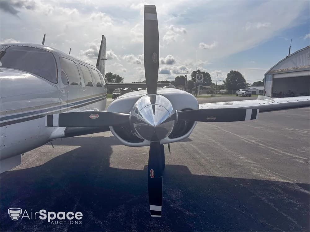 A close-up, head-on view of the right propeller and engine cowling of a white Piper Navajo aircraft.