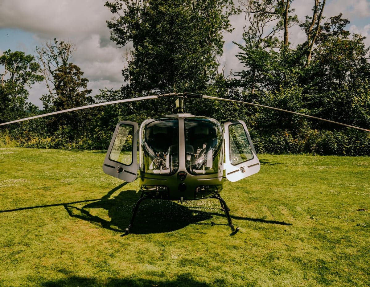 Front view of a helicopter with open doors on a grassy field.