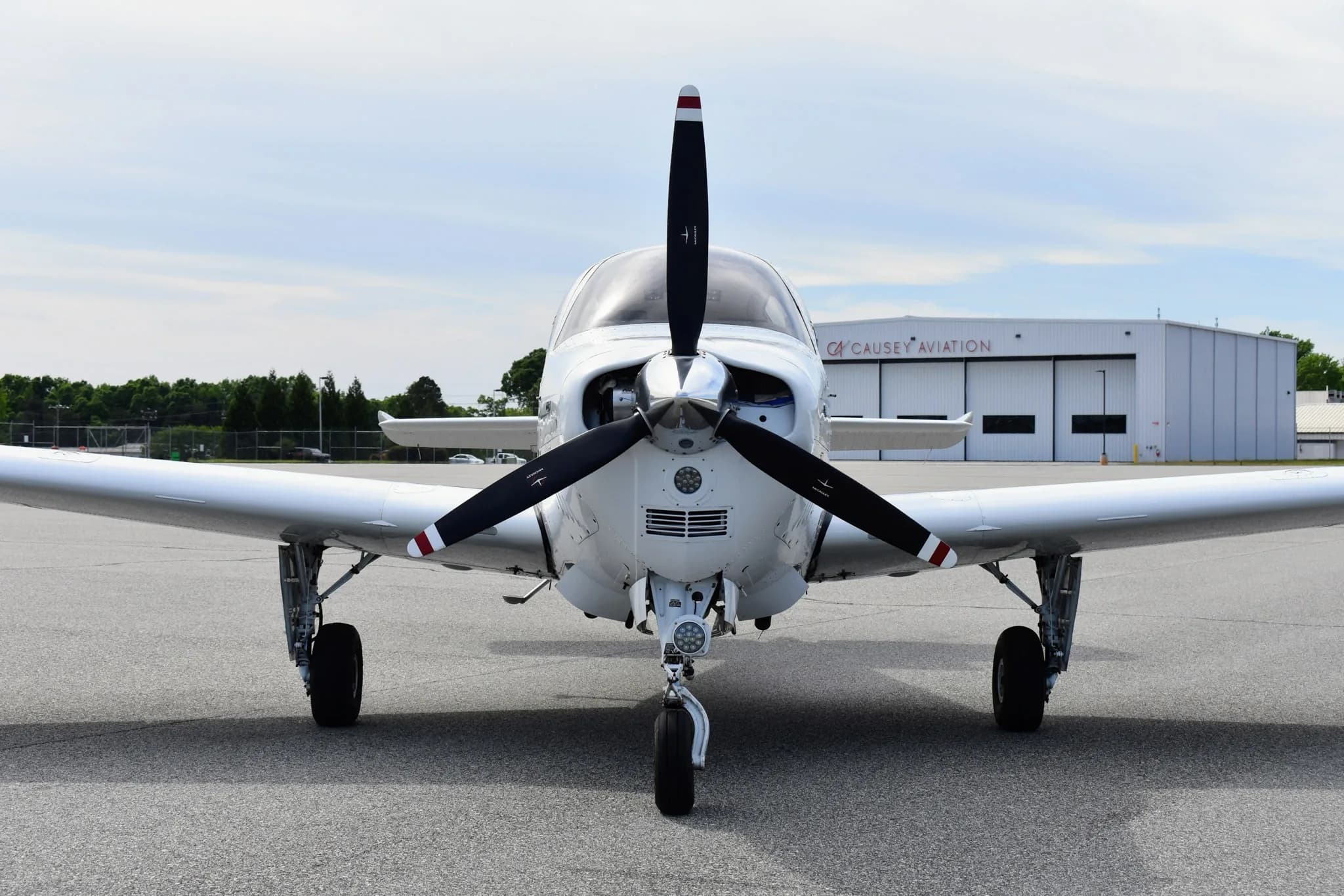A close-up front view of a white Beechcraft Bonanza F33A with a three-bladed propeller.